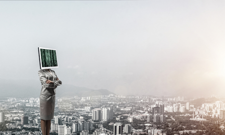 Cropped image of business woman in suit with monitor instead of head keeping arms crossed while standing outdoors with cityscape view on background.の写真素材
