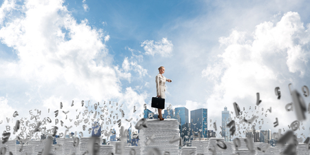 Confident business woman in suit standing among flying letters with cloudly skyscape on background. Mixed media.の写真素材