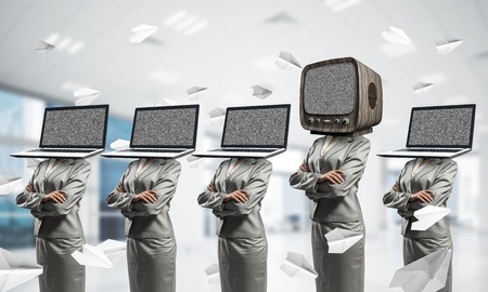 Business women in suits with laptops instead of their heads keeping arms crossed while standing in a row and one at the head with old TV inside office building.の写真素材