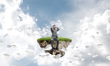 Frustrated businessman sitting on green island and closing ears with handsの写真素材