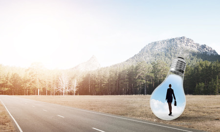 Young businesswoman trapped inside of light bulb on asphalt roadの写真素材