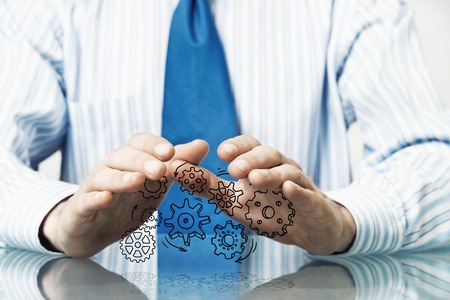 Close up of businessman sitting at table and protecting gear mechanism with palmsの写真素材