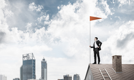 Businessman standing on house roof and red holding flag. Mixed mediaの写真素材