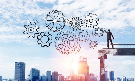 Businessman in suit drawing sketches of gear mechanism while standing on broken bridge with cityscape and sunlight on background. 3D rendering.の写真素材