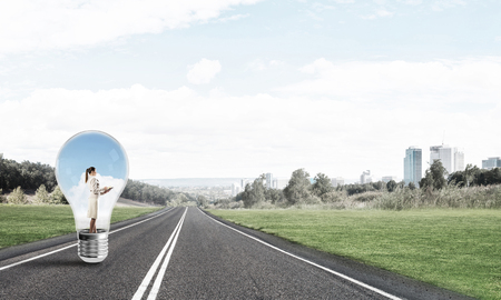 Young businesswoman trapped inside of light bulb on asphalt roadの写真素材