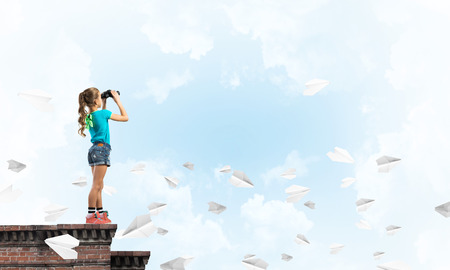Cute girl of school age on building roof looking in binocularsの写真素材