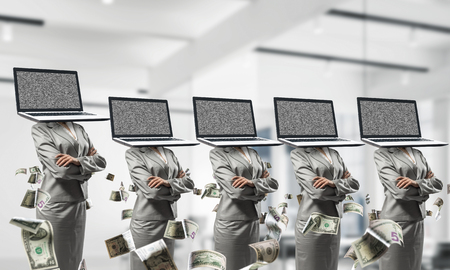 Business women in suits with laptops instead of their heads keeping arms crossed while standing in a row among flying dollar banknotes inside office building.の写真素材