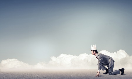 Young handsome businessman wearing white paper crown running in a hurryの写真素材