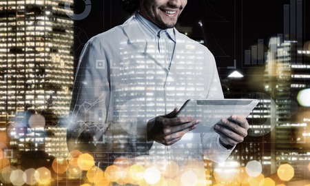 Double exposure of confident doctor in white sterile coat and night modern cityscape view on...