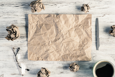 Top view of modern creative workplace with creased piece of sheet, pen, crumpled paper balls and cup of coffee placed on wooden table. Concept of finding of outstanding idea.の写真素材