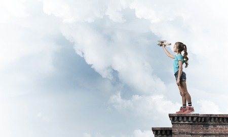 Cute happy kid girl on building top playing with retro plane modelの写真素材