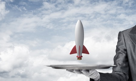 Cropped image of waitress's hand in white glove presenting flying missile on metal tray with cloudy skyscape on background.の写真素材