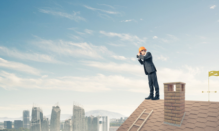 Young businessman in suit and helmet on roof edge in search of something new. Mixed mediaの写真素材