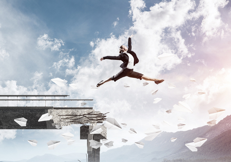 Business woman jumping over gap in bridge among flying paper planes as symbol of overcoming challenges. Skyscape with sunlight and nature view on background. 3D rendering.の写真素材