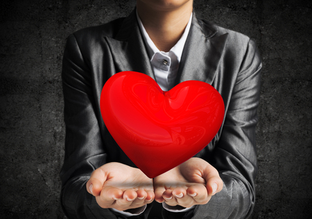 Cropped image of businessman in suit presenting big red heart his hands with dark wall on background. 3D rendering.の写真素材