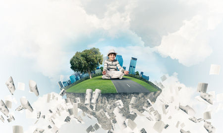 Young little boy keeping eyes closed and looking concentrated while meditating on flying island among flying papers with cloudy skyscape on background. 3D rendering.の写真素材