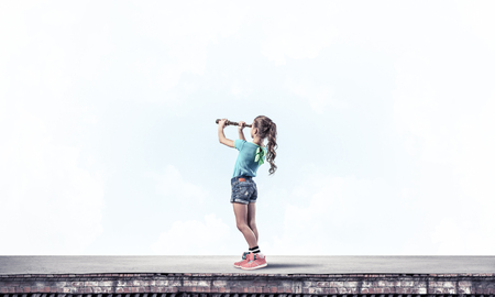 Cute kid girl standing on house roof and looking in spyglassの写真素材
