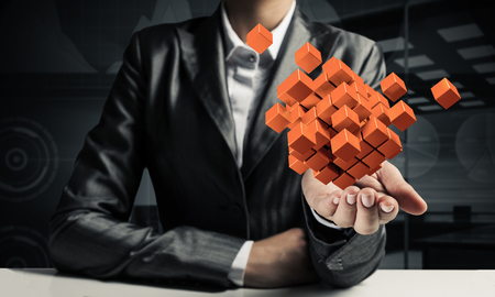 Cropped image of business woman in suit presenting multiple cubes in hand as symbol of innovations. Dark office view on background. 3D rendering.の写真素材