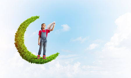 Cute kid girl standing on green moon playing with airplane toyの写真素材