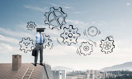 Faceless businessman with camera zoom instead of head standing on house roofの写真素材