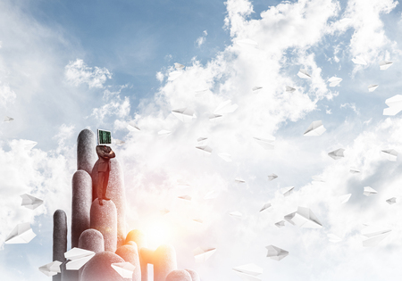 Businessman in suit with monitor instead of head keeping arms crossed while standing on the top of stone columns among flying paper planes with beautiful landscape on background. 3D rendering.の写真素材