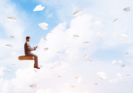 Young businessman sitting on old book with mobile phone in hands