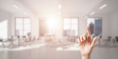 Close of woman hand touching screen with finger and office at backgroundの写真素材