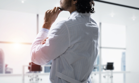 Cropped image of confident doctor in white sterile coat standing inside white hospital office building with sunlight on background.の写真素材