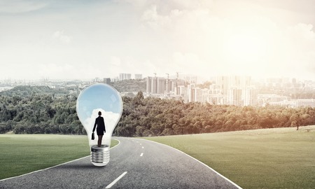 Young businesswoman trapped inside of light bulb on asphalt roadの写真素材