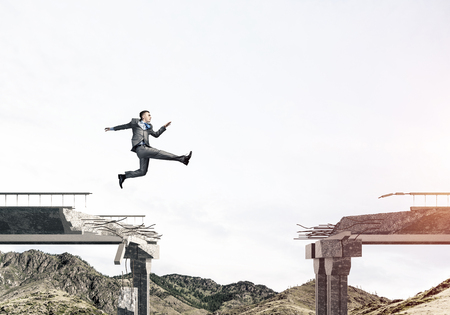 Businessman jumping over huge gap in concrete bridge as symbol of overcoming challenges. Skyscape and nature view on background. 3D rendering.の写真素材