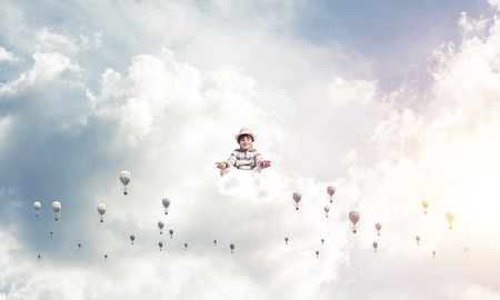 Young little boy keeping eyes closed and looking concentrated while meditating among flying balloons in the air with cloudy skyscape on background.の写真素材