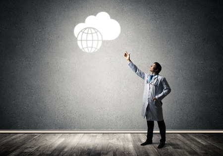 Professional medical industry employee interracting with conceptual glowing cloud while standing inside empty room and gray wall on background.の写真素材