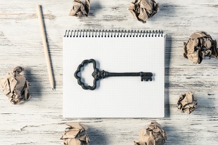 Top view of modern creative workplace with key on notepad, pencil and crumpled paper balls placed on wooden table. Concept of finding of outstanding idea.の写真素材