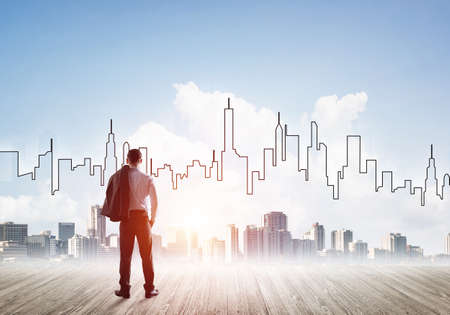 Businessman standing with back and looking at silhouette of modern business centerの写真素材
