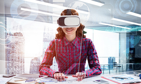 Horizontal shot of young and beautiful woman in checkered shirt using VR headset and media interface...