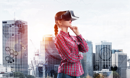 Young caucasian woman in virtual reality helmet against cityscape backgroundの写真素材