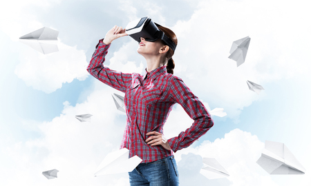 Young caucasian woman in virtual reality helmet against sky backgroundの写真素材