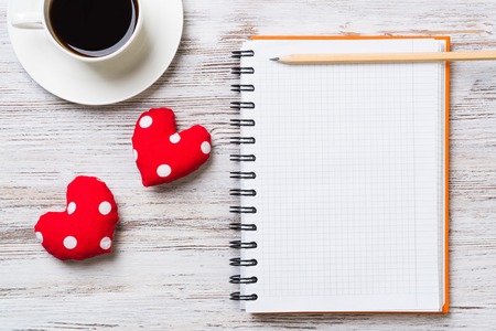 Coffee cup notepad pencil and two red hearts on wooden surfaceの写真素材