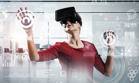 Beautiful and young woman in red dress using virtual reality headset with digital media structure...