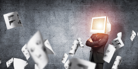 Businessman in suit with monitor instead of head keeping arms crossed while standing among flying papers and against gray dark wall on background.の写真素材