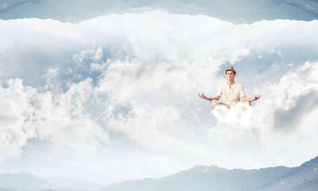 Young man keeping eyes closed and looking concentrated while meditating on cloud in the air between two nature worlds.の写真素材