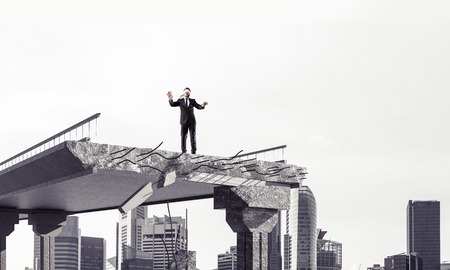 Businessman walking blindfolded on concrete bridge with huge gap as symbol of hidden threats and risks. Cityscape view on background. 3D rendering.の写真素材