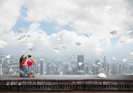 Cute girl of school age on building roof looking in binocularsの写真素材