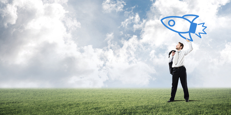 Young and confident businessman in suit launching big blue rocket from his hand.の写真素材