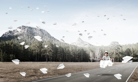 Young little boy keeping eyes closed and looking concentrated while meditating on cloud above the road with beautiful and breathtaking landscape on background.の写真素材