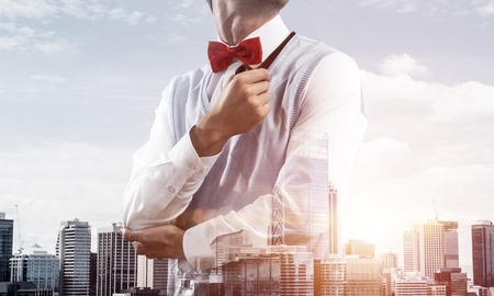 Double exposure of confident and young businessman in smart-casual wear smoking pipe and modern cityscape on background. Concept of young and successful entrepreneur.の写真素材