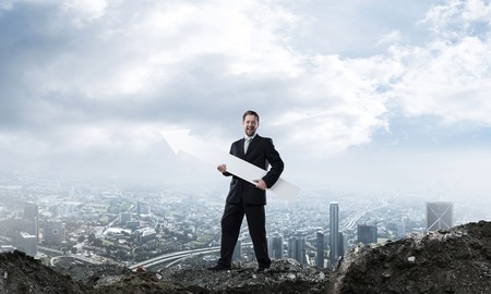 Confident and young businessman in suit holding huge white arrow which pointing away as symbol of development and improvement. Cityscape view and cloudy sky on backgroundの写真素材