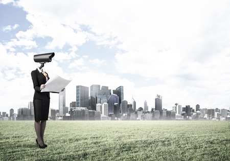 Elegant businesswoman outdoors with papers in hands and camera instead of headの写真素材