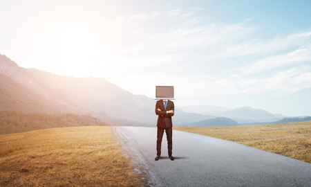 Businessman in suit with laptop instead of head keeping arms crossed while standing on the road with beautiful landscape on background.の写真素材
