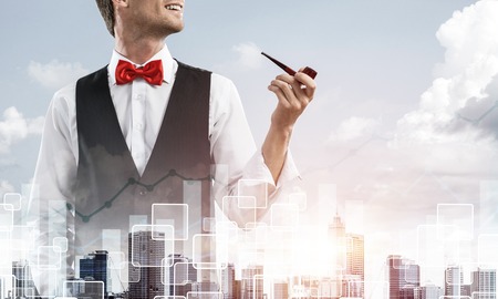 Double exposure of confident and young businessman in smart-casual wear smoking pipe and modern cityscape with business and media interface. Concept of new technologies for modern business.の写真素材